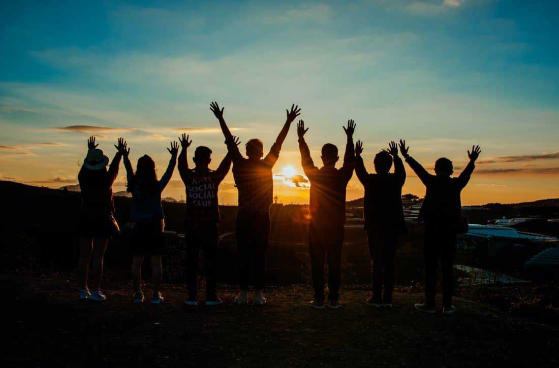 Group of people looking at the sunset with arms raised.